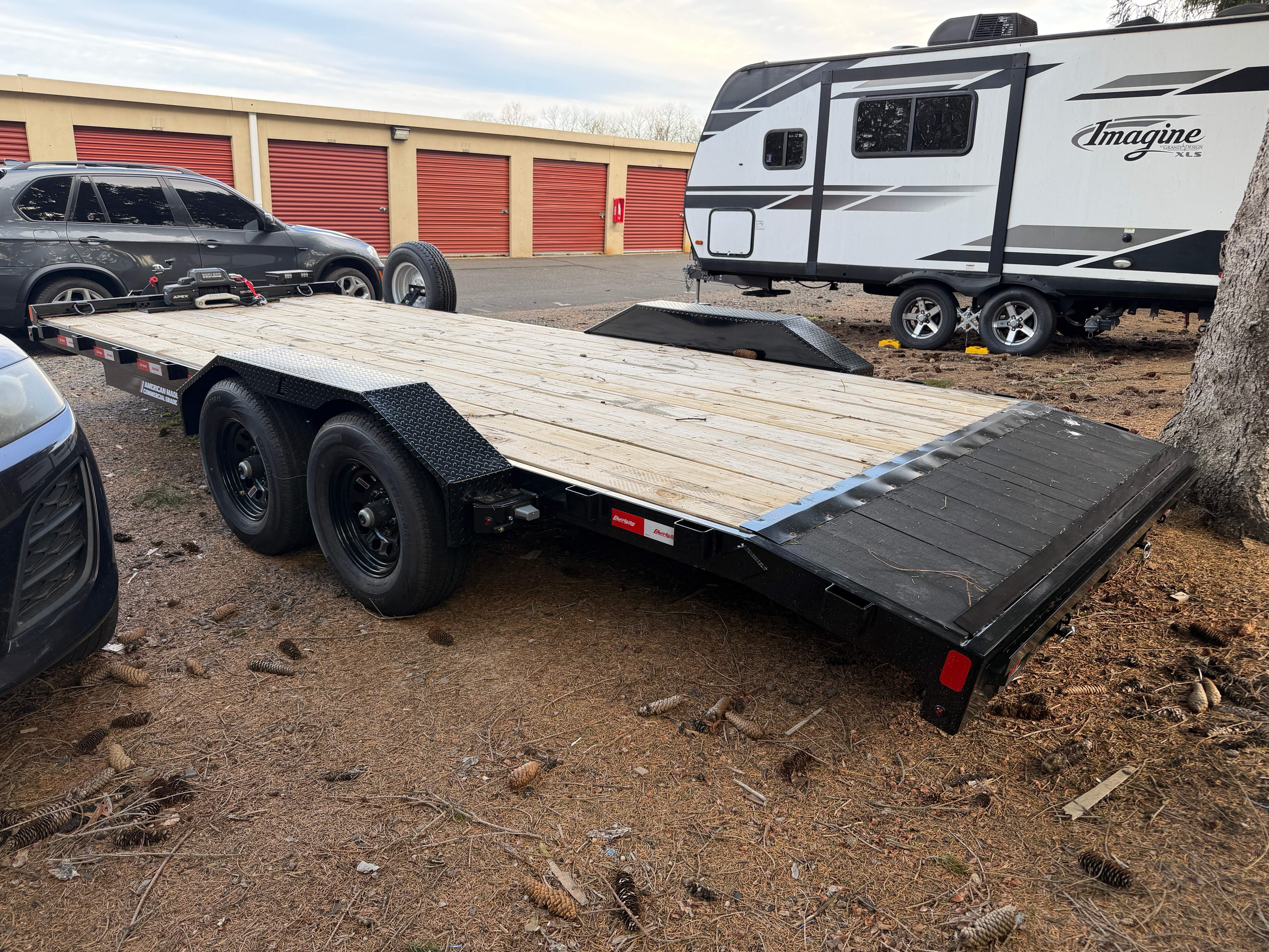 Thumbnail: Side profile view of car hauler trailer showing wood deck, dual axles with electric brakes, and safety chains